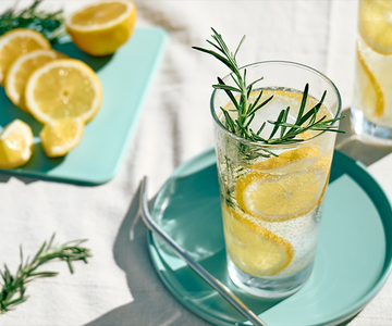 Ein Glas Zitonensirup mit Zitronenscheiben und Rosmarinzweigen.