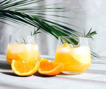 Zwei Gläser Orangensirup mit Eis und Rosmarinzweigen.