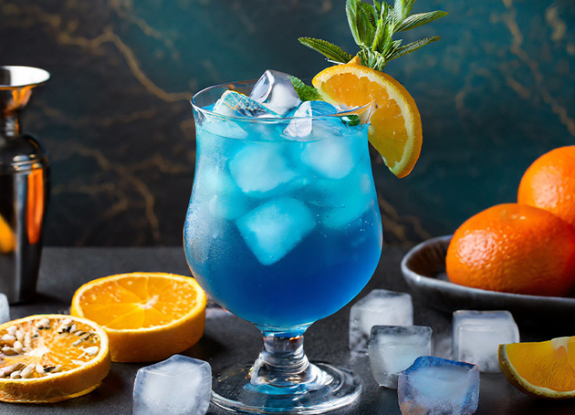 Ein blauer Cocktail mit Orangenscheiben und Eis.