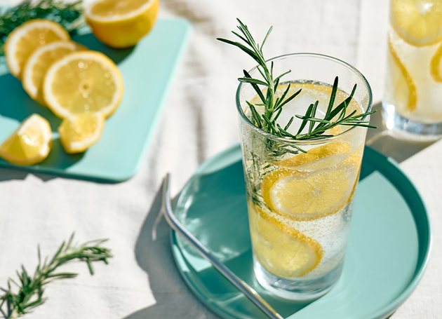 Ein Glas Zitonensirup mit Zitronenscheiben und Rosmarinzweigen.