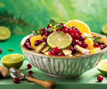 Eine grüne Schüssel mit Obstsalat aus Orangen, Preiselbeeren und Ingwer auf einem Tisch.