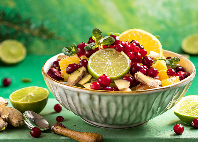 Eine grüne Schüssel mit Obstsalat aus Orangen, Preiselbeeren und Ingwer auf einem Tisch.