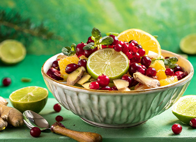 Eine grüne Schüssel mit Obstsalat aus Orangen, Preiselbeeren und Ingwer auf einem Tisch.