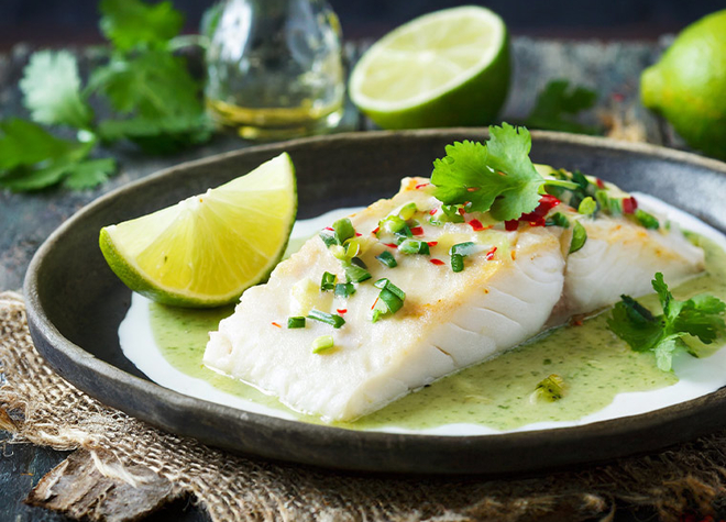 Ein schwarzer Teller mit Fisch mit Limettensauce und Limettenspalten.