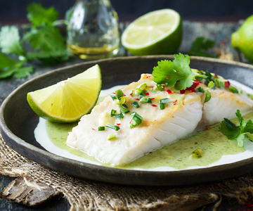 Ein schwarzer Teller mit Fisch mit Limettensauce und Limettenspalten.