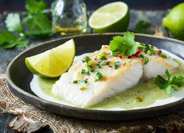 Ein schwarzer Teller mit Fisch mit Limettensauce und Limettenspalten.