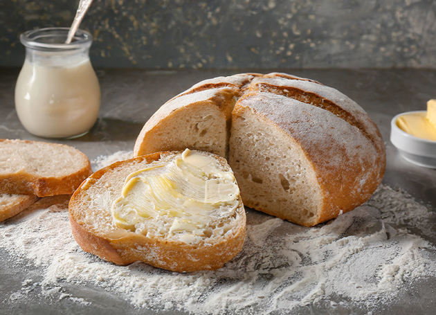 Ein Laib Brot mit einer abgeschnittenen Scheibe mit Butter und ein Glas Milch.