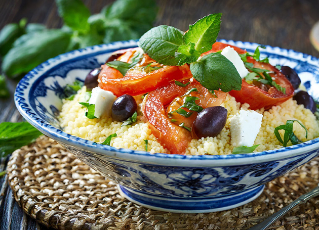 Eine blaue Schüssel Couscous mit Tomaten und Oliven.