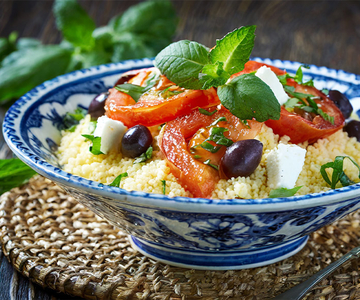 Eine blaue Schüssel Couscous mit Tomaten und Oliven.