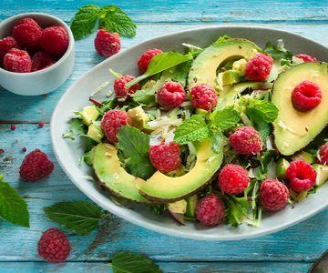 Avocadosalat mit Himbeeren und Avocado in einer Schüssel auf einem blauen Holztisch.