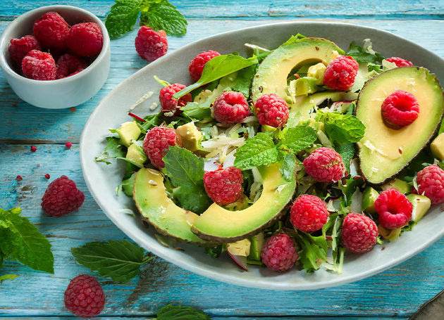 Avocadosalat mit Himbeeren und Avocado in einer Schüssel auf einem blauen Holztisch.