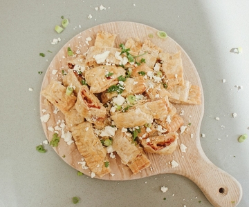 Blätterteig Stückchen mit Feta-Käse auf einem hölzernen Schneidebrett