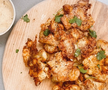 Gebratene zerschlagene Kartoffeln auf einem Holzschneidebrett. Daneben ist eine Schüssel mit Knoblauch-Dip