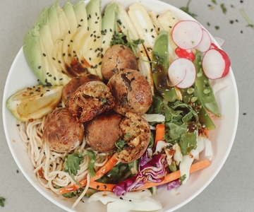 Eine Schüssel Nudeln mit Auberginenkroketten, Avocado, Kohl und Radieschen.