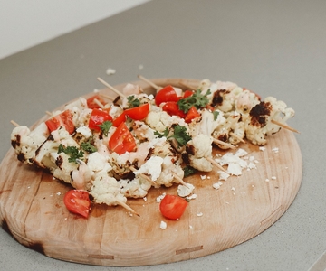 Gegrillte Blumenkohlspieße mit Cherrytomaten auf einem Holzbrett.