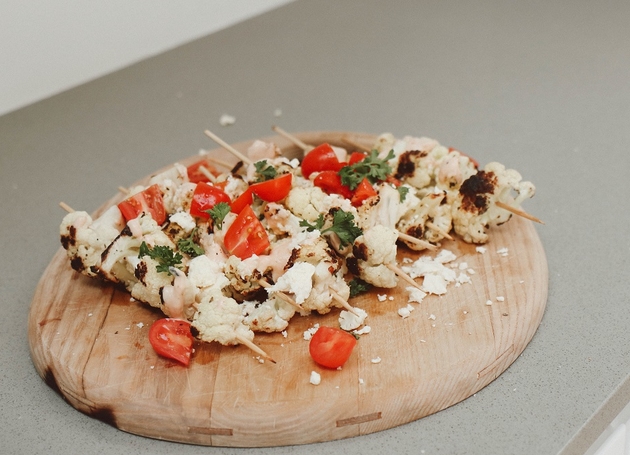 Gegrillte Blumenkohlspieße mit Cherrytomaten auf einem Holzbrett.