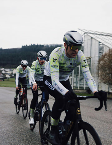 Drei Radfahrer in passender Cycling Team Ost Teamkleidung fahren auf einer Straße.