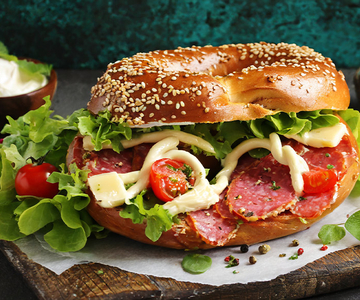 Ein Bagel mit Wurst, Salat, Tomaten und Mayonaise.