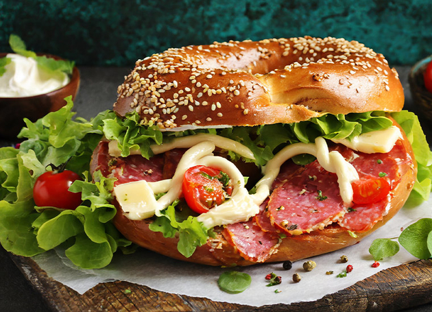 Ein Bagel mit Wurst, Salat, Tomaten und Mayonaise.