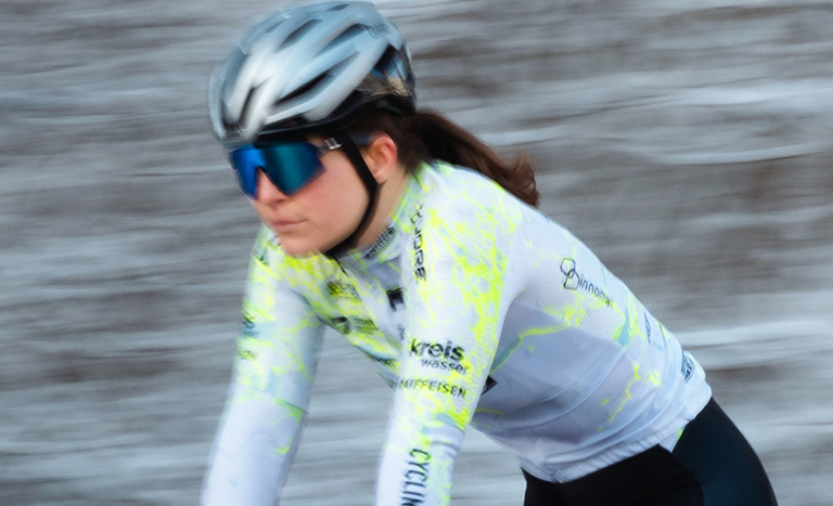 Radfahrerin mit Helm und Trikot fährt durch eine verschneite Waldlandschaft.