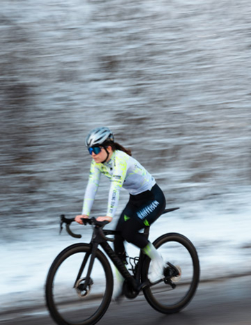 Radfahrerin des Cycling Team Ost fährt durch eine verschneite Waldlandschaft.