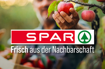 Eine verschwommene Aufnahme von einem Mann der einen Apfel pflückt und davor ist das SPAR-Logo.