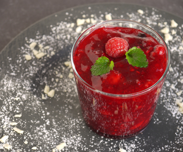 Ein Glas mit Erdbeergrütze mit Melonen und Himbeeren ganiert mit Puderzucker.