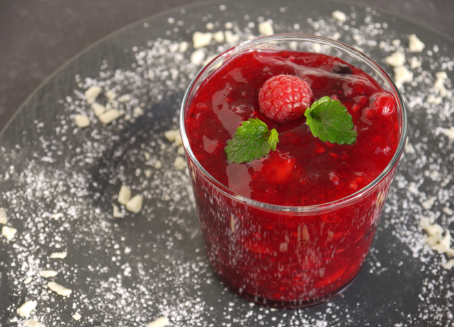 Ein Glas mit Erdbeergrütze mit Melonen und Himbeeren ganiert mit Puderzucker.