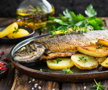 Ein gebratener Fisch mit Kartoffelscheiben und Kräutern auf einem Teller.