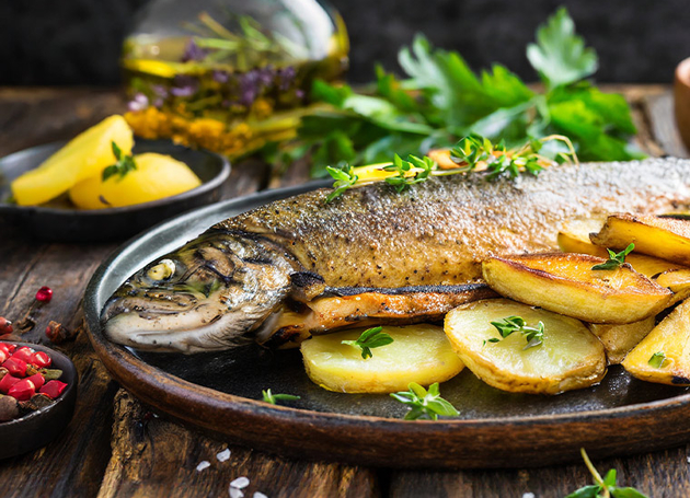 Ein gebratener Fisch mit Kartoffelscheiben und Kräutern auf einem Teller.