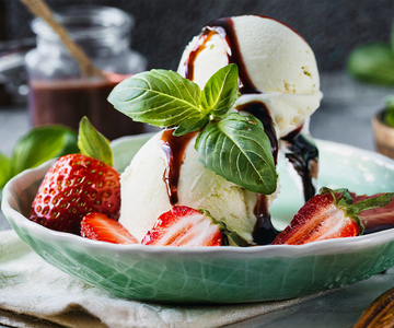 Eine grüne Schüssel mit Basilikumglace mit Erbeeren, Minze und Balsamico Topping..