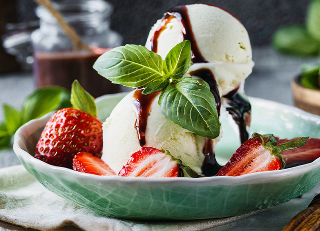 Eine grüne Schüssel mit Basilikumglace mit Erbeeren, Minze und Balsamico Topping..