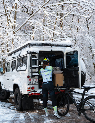 Radfahrerin bereitet sich auf eine Fahrt bei Schnee in der Nähe eines Fahrzeugs vor.