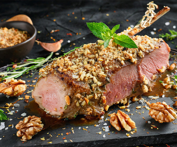 Gebratenes Lammfilet in Nusskruste und Kräutern auf einer schwarzen Schiefertafel.
