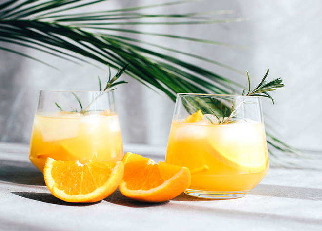 Zwei Gläser Orangensirup mit Eis und Rosmarinzweigen.