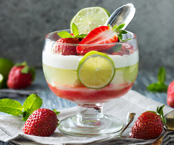 Ein Erdbeer-Limetten-Parfait in einem Glas mit einem Löffel, garniert mir Erdbeeren und Limettenscheiben..