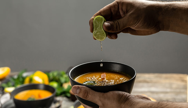 Eine Person presst eine Limette in eine Schüssel Suppe aus.