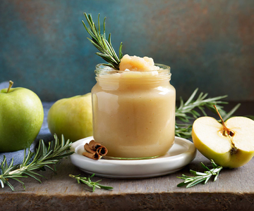 Apfelkompott im Glas mit Äpfeln und Rosmarinzweigen drumherum.