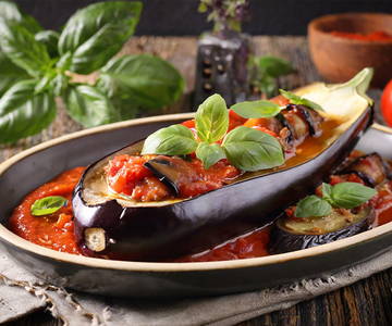 Gefüllte Aubergine mit Tomatensauce und Basilikum auf einem Holztisch.