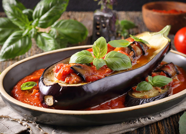 Gefüllte Aubergine mit Tomatensauce und Basilikum auf einem Holztisch.