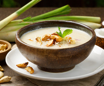 Eine Schüssel mit Kokos-Ztironengrass-Suppe auf einem Tisch neben einer Schüssel mit Cashew-Nüssen.