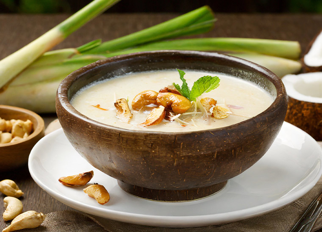 Eine Schüssel mit Kokos-Ztironengrass-Suppe auf einem Tisch neben einer Schüssel mit Cashew-Nüssen.
