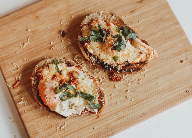 Zwei Scheiben Brot mit Pesto und Spiegeleiern auf einem Holzschneidebrett.