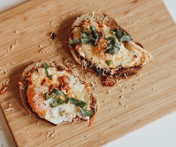 Zwei Scheiben Brot mit Pesto und Spiegeleiern auf einem Holzschneidebrett.