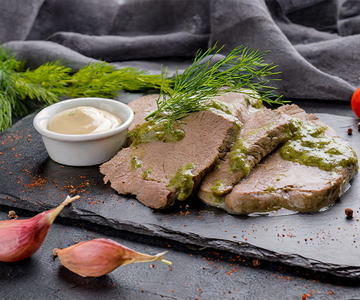 Scheiben Siedfleisch vom Rind auf einer Schieferplatte mit Dill-Sauce beträufelt.