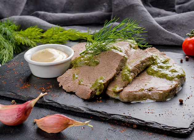 Scheiben Siedfleisch vom Rind auf einer Schieferplatte mit Dill-Sauce beträufelt.