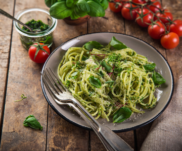 Ein Teller mit Spaghetti mit Selleriesauce mit Tomaten und Basilikum auf einem Holztisch.