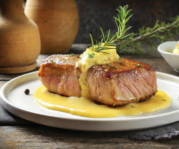 Ein Teller mit einem Stück Entrecote-Fleisch mit Soße und Rosmarin darauf.