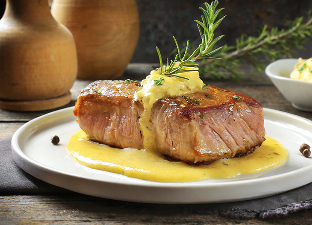 Ein Teller mit einem Stück Entrecote-Fleisch mit Soße und Rosmarin darauf.