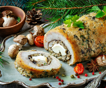 Eine Roulade mit Pilzen und Fisch auf einem Servierplatte. Im Hintergrund sind Pilze und Baumnadeln  
